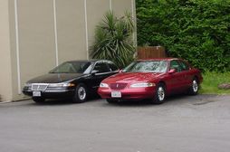 A 1994 Lincoln Mark VIII (black) and a 1997 Lincoln Mark VIII LSC (Toreador Red). These represent the First and Second generations of the FN10 platform, respectively